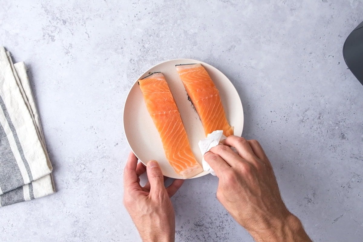 hand with paper towel patting salmon patty dry on counter.