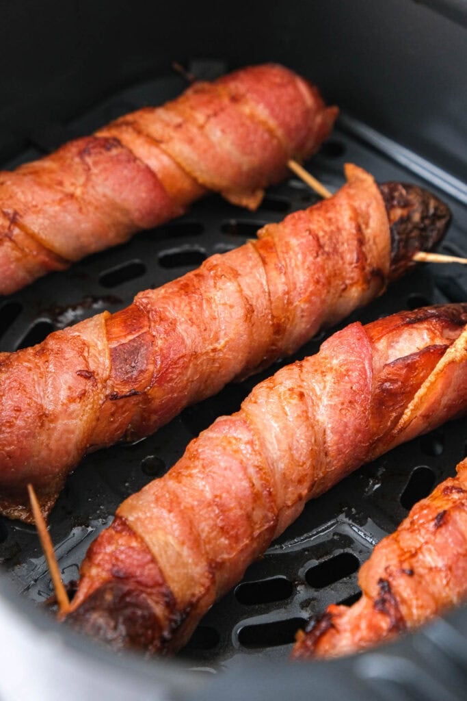 bacon wrapped hot dogs in air fryer in basket.