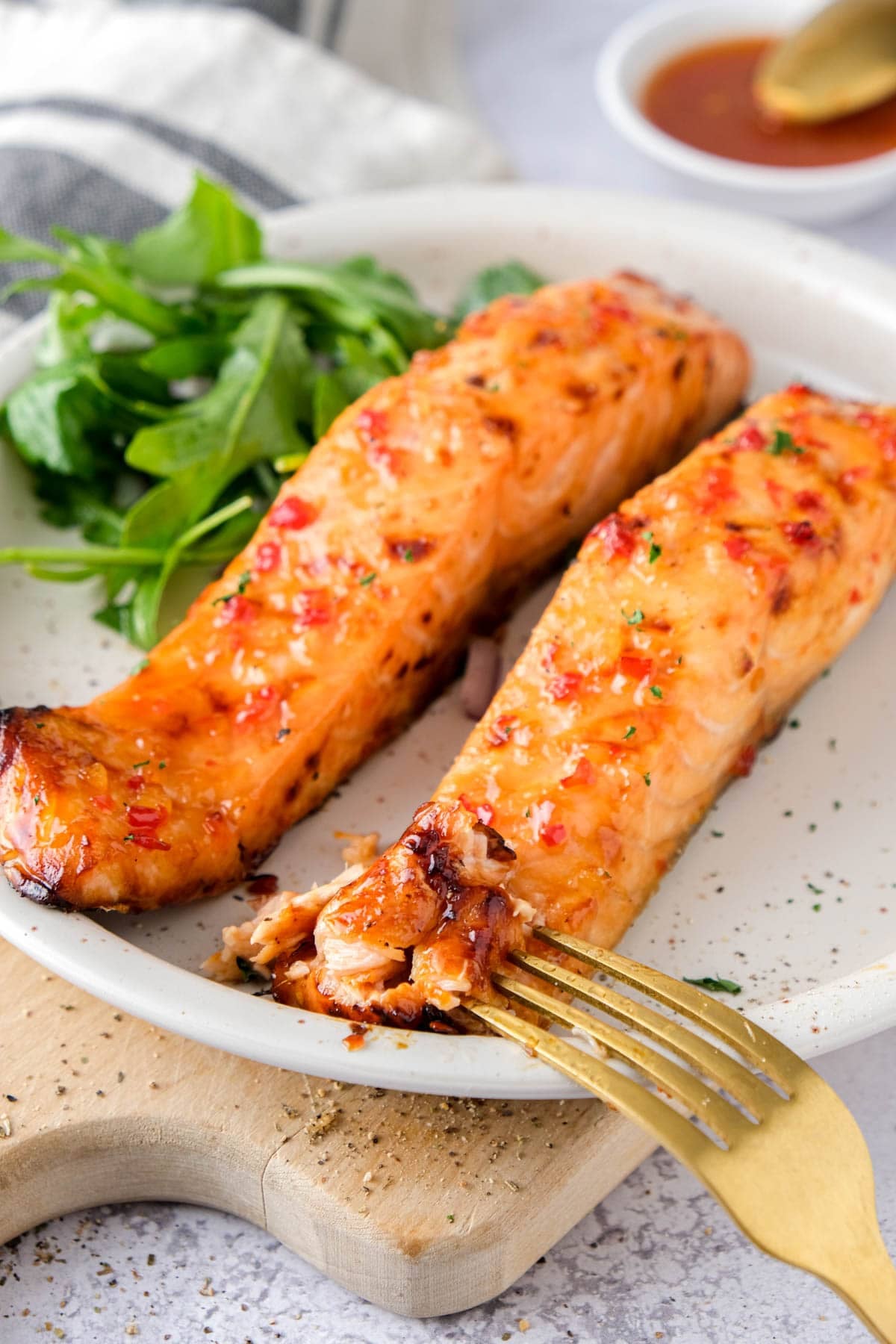 two sweet chili salmon fillets on plate with golden fork eating some.