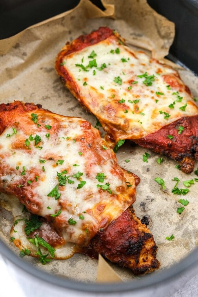 chicken parmesan on parchment paper in air fryer basket.