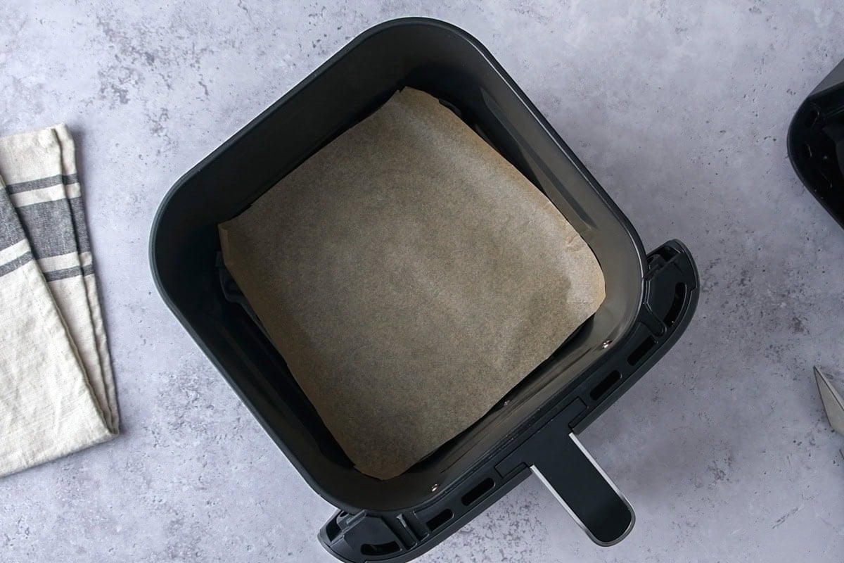 air fryer basket on counter with parchment paper cut inside.
