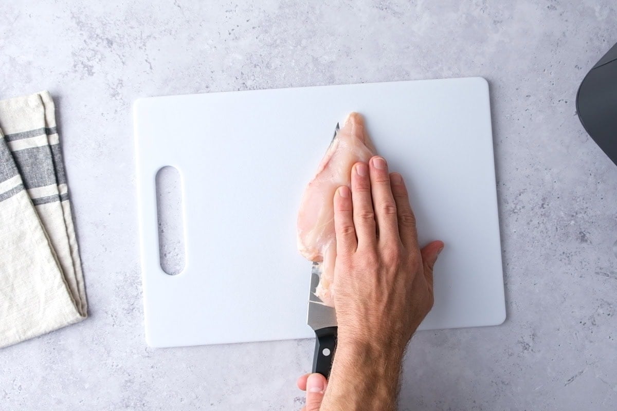 hand holding piece of chicken breast being cut with a knife.