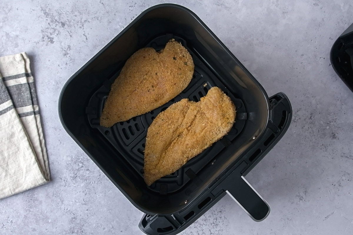 breaded chicken breasts in air fryer basket on counter.