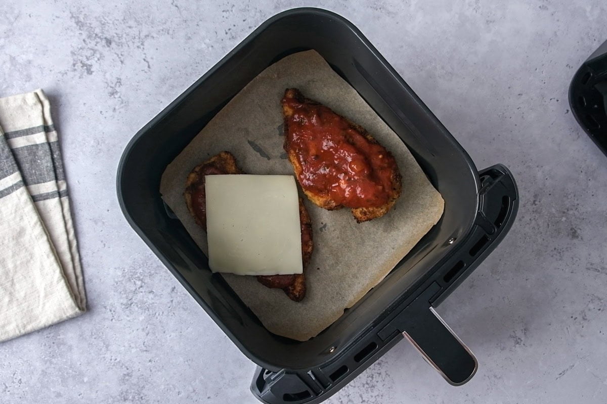 slice of mozzarella cheese on chicken breast covered in sauce in air fryer.