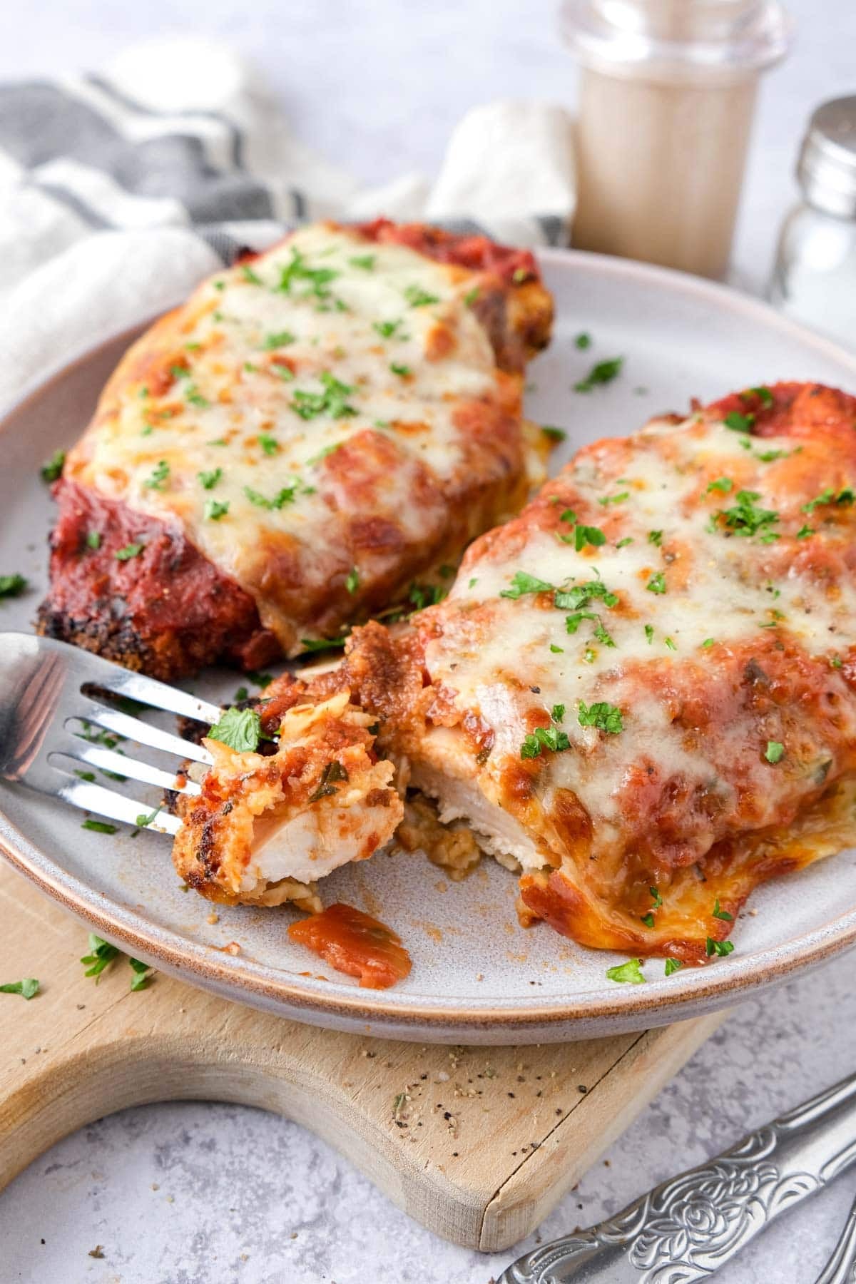 fork holding piece of cut chicken parmesan on plate with parsley on top.