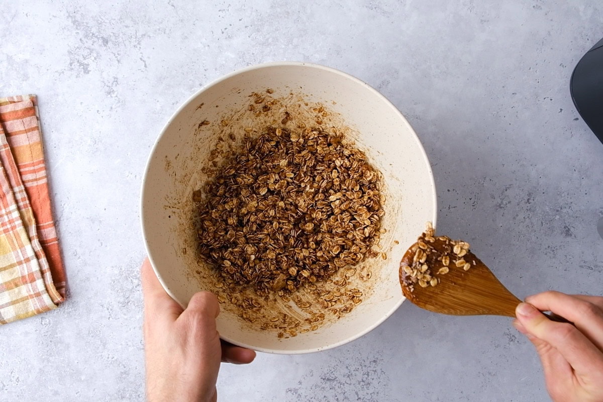 hand holding wooden spoon mixing cinnamon and oats in large bowl.
