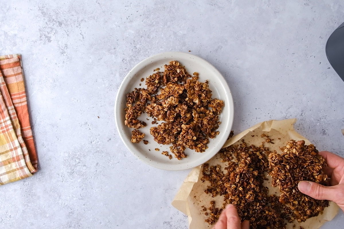 hand breaking up granola into chunks and adding them to a plate.