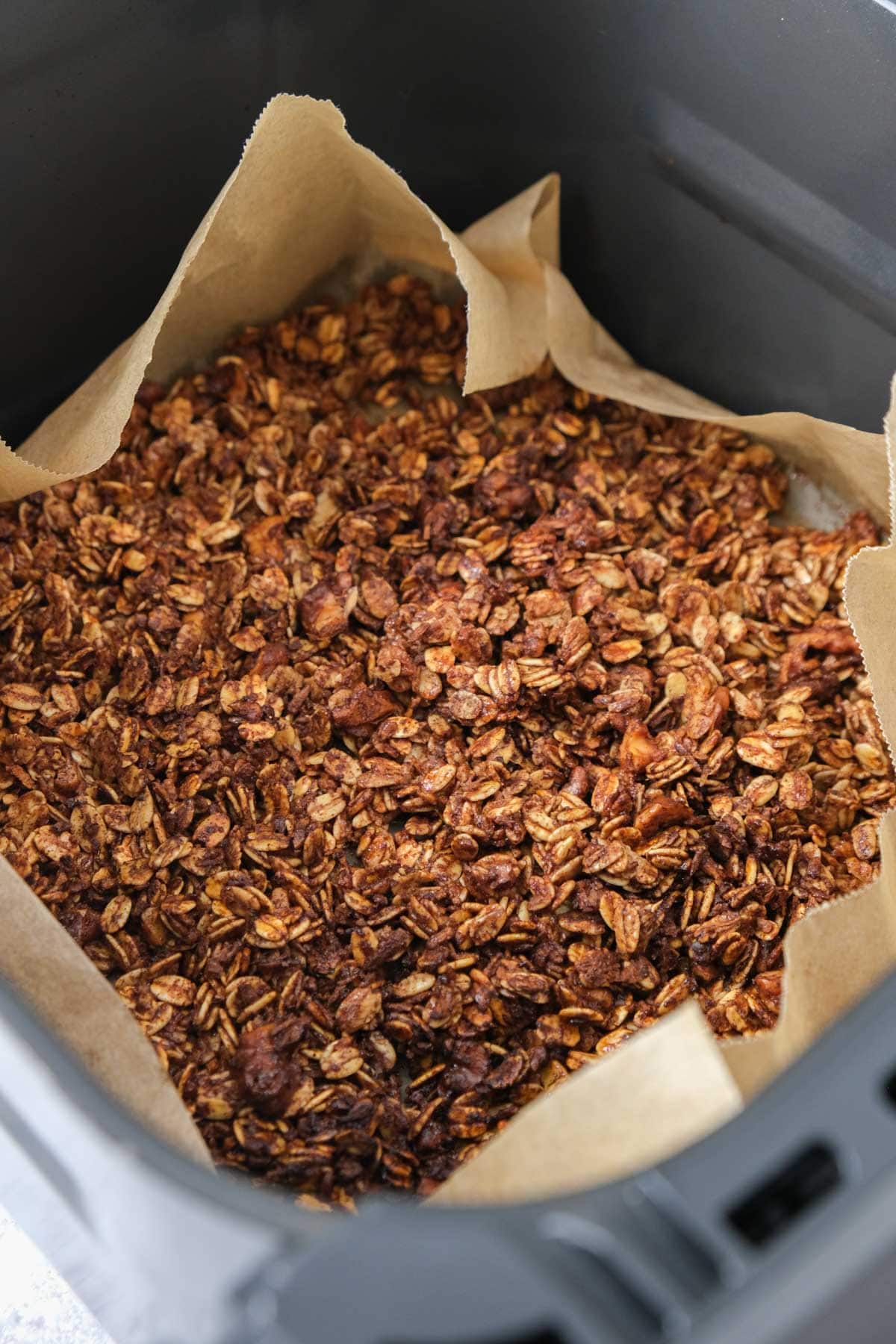 crispy air fryer granola in air fryer basket on parchment paper.