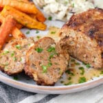 meatloaf cut up on a plate with sides behind.