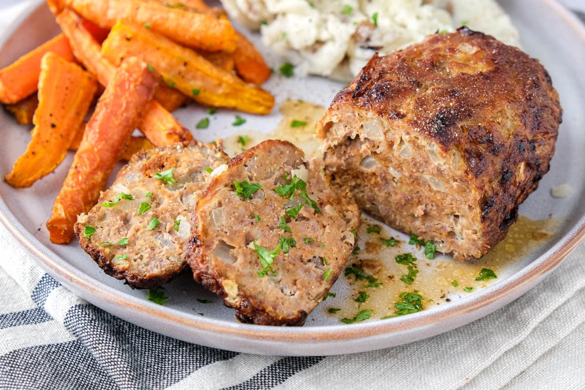 meatloaf cut up on a plate with sides behind.