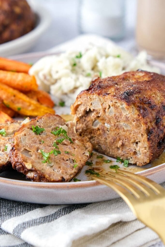 mini meatloaf on plate with slice removed and vegetables on plate behind.