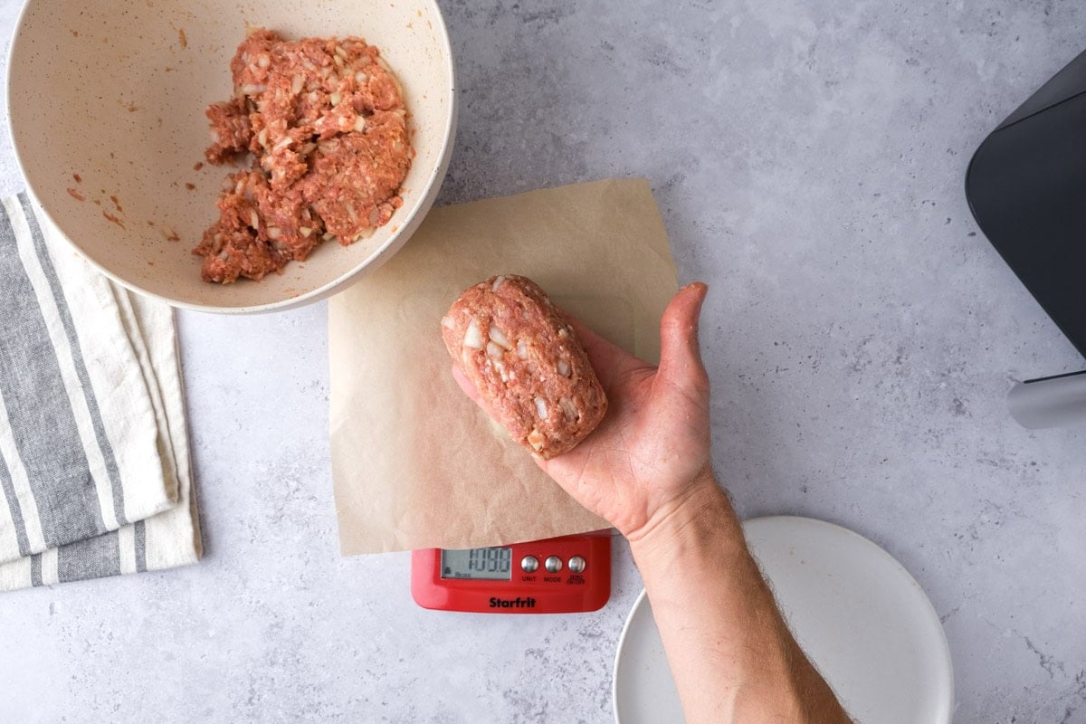hand holding formed mini meatloaf above scale on counter.
