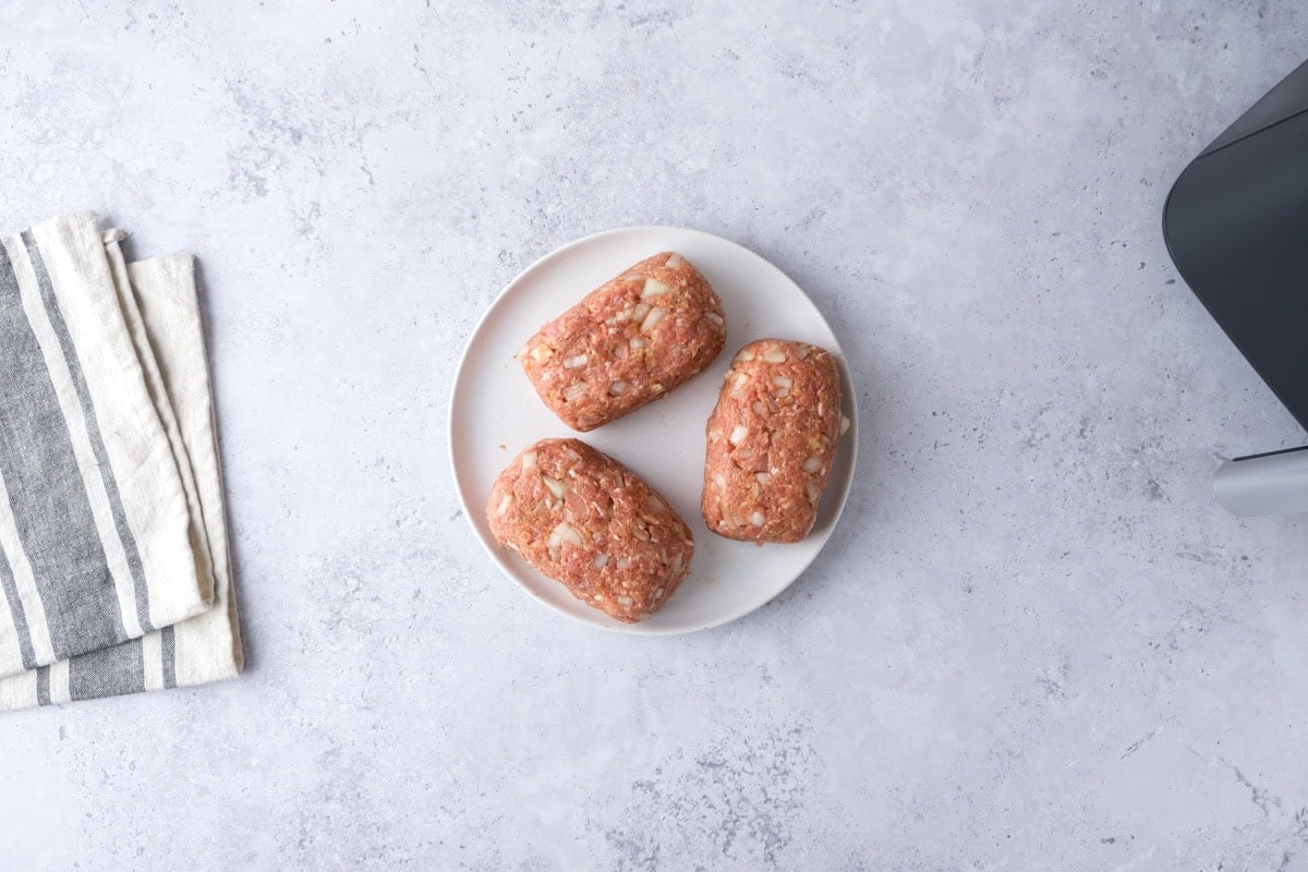 three raw mini meatloaves on plate on counter.