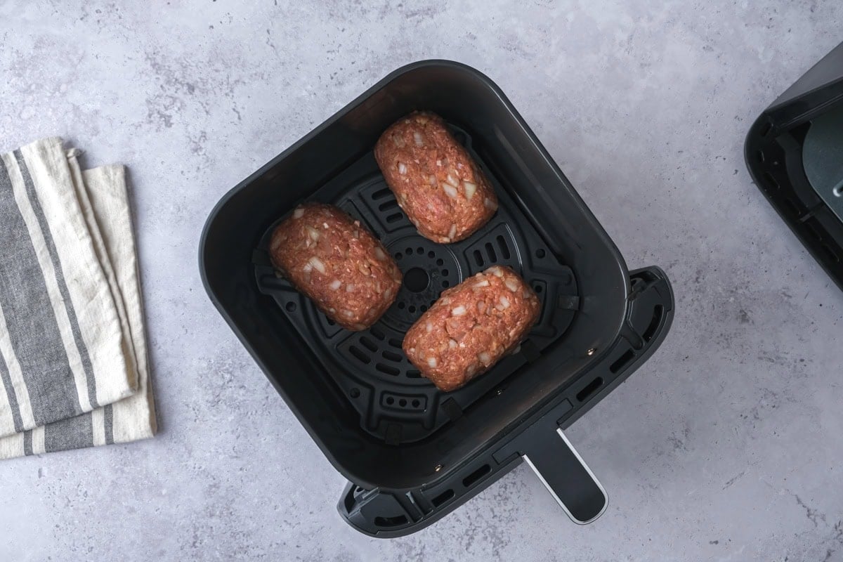 raw mini meatloaves in air fryer basket on counter.