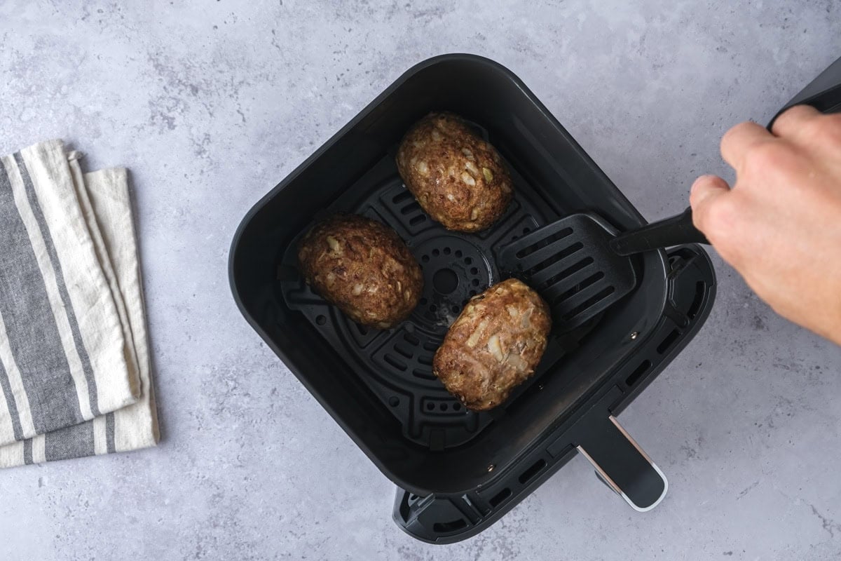 black flipper flipping mini meatloaves in air fryer basket.
