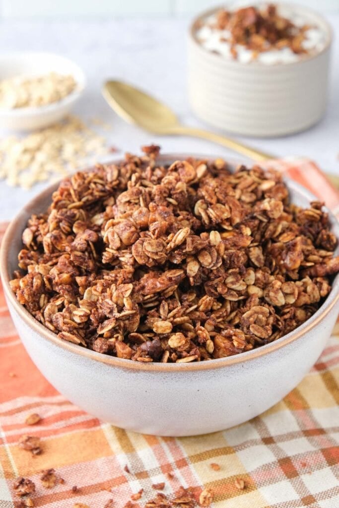 bowl of homemade granola on fall cloth with oats behind.